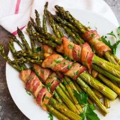 asparagus wrapped in bacon on a white plate with parsley garnish