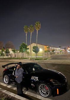 a woman standing next to a black sports car on the side of a road at night