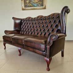 a brown leather couch sitting on top of a tile floor next to a painting hanging on the wall