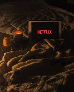 a netflix sign sitting on top of a bed next to two candles and some blankets