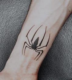 a small black spider tattoo on the left forearm and wrist, with an arrow in the center