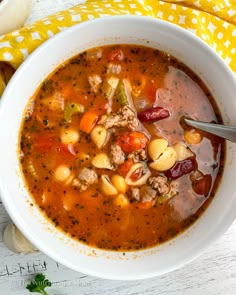 a white bowl filled with meat and vegetable soup on top of a yellow towel next to a spoon