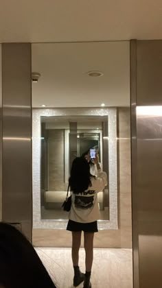 a woman taking a selfie in an elevator with her cell phone up to her ear