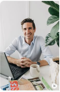 a man sitting in front of a laptop computer on top of a white desk next to a potted plant