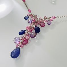 Semiprecious gemstones of Tanzanite, Pink Sapphire and Light Amethyst are nestled between smaller Mystic Pink Topaz and Mystic Pink Quartz rondelles. The large focal tanzanite measures approximately 12 mm long by 9 mm wide. The other gemstone briolettes range from 6 mm to 10 mm long or wide. All of the gemstones have beautiful color saturation. This necklace is finished in sterling silver and measures approximately 16¼ to 20¼-inches long with the 4-inch extender. The pendant falls approximately 1¾-inches from the necklace. Matching earrings are available upon request. Find more beautiful styles at my Etsy store or www.blueeasel.etsy.com. Item ships in a leatherette jewelry box with Blue Easel Designs logo via USPS Priority Mail with Delivery Confirmation and shipping insurance. ID#E03?? Tanzanite Briolette Gemstone Necklace, Fine Jewelry Pink Multi-stone Necklace, Tanzanite Briolette Necklace Gift, Sapphire Gemstone Drop Necklaces, Sapphire Drop Gemstone Necklace, Briolette Tanzanite Necklace For Gift, Sapphire Drop Necklace With Gemstone, Amethyst Multi-stone Briolette Gemstones, Amethyst Briolette Multi-stone Gemstones