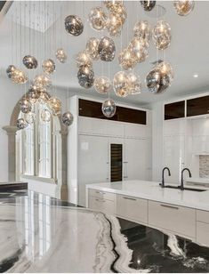 a large kitchen with marble counter tops and lights hanging from the chandelier above it