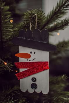 a wooden snowman ornament hanging from a christmas tree with red glitter ribbon