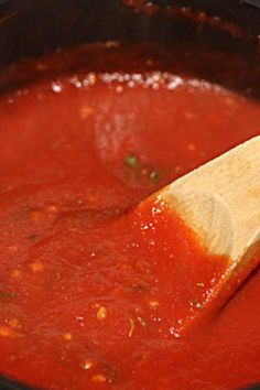 a wooden spoon in a pot filled with tomato sauce