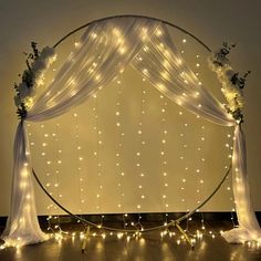 an arch decorated with lights and flowers on top of a wooden floor in front of a wall