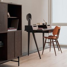 a desk with a chair and bookshelf in an office space that is well lit by the window