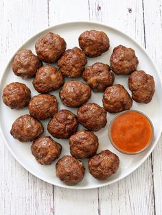 meatballs and sauce on a white plate next to a small bowl of ketchup