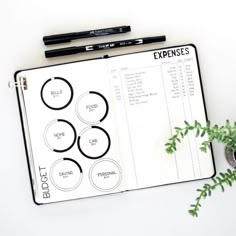 an open planner with circles on it next to a potted plant and two pens