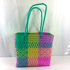 a multicolored woven tote bag sitting on top of a white table next to a wall