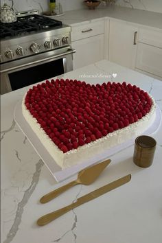 a heart - shaped cake with raspberries on it sits on a counter next to utensils