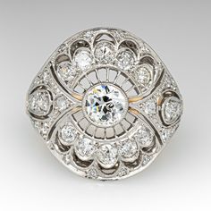 This elegant ring features a platinum gallery with a pierced design and is bordered with milgrain edging. The ring is centered with one (1), bezel set, old European cut diamond. The ring is also accented with thirty-four (34), bead set, old European/single cut diamonds. The ring is finished with an 18K yellow gold shank. The ring measures 21.3mm at the top, rises 6.9mm above the finger, tapering to 2.6mm wide and 1.0mm thick at the base of the shank. This ring is currently a size 6.25. Art Deco Diamond White Ring With Bezel Setting, Art Deco White Diamond Ring With Bezel Setting, Round Cut Diamond Ring With Milgrain Detail, Art Deco White Gold Diamond Ring With Bezel Setting, Luxury Platinum Filigree Ring With Single Cut Diamonds, Timeless Diamond Rings With Milgrain Detail, White Gold Diamond Ring With Milgrain Detail, Luxury Milgrain Round Diamond Ring, Luxury Round Milgrain Diamond Ring