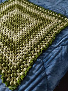 a green and white crocheted blanket laying on top of a blue bedspread