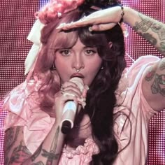 a woman with long hair holding a microphone in front of her head and wearing a pink dress