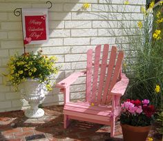 a pink adirondack sitting in front of a brick wall with potted flowers