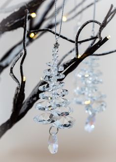 three crystal ornaments hanging from a tree with lights in the background and branches to the side