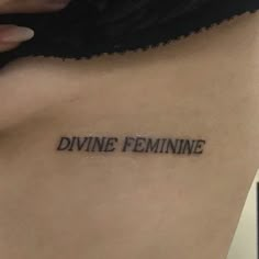 a woman's back with the word divine feminine tattooed on her left side ribcage