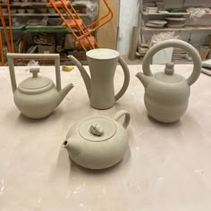 three teapots are sitting on a table in front of some other pottery items