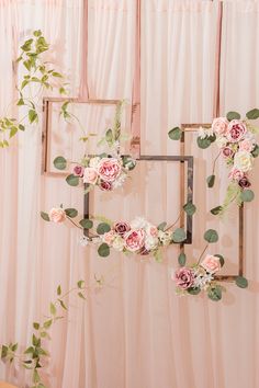 an arrangement of flowers and greenery hangs on the wall in front of a pink backdrop