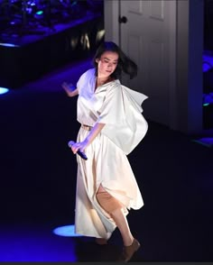 a woman in a white dress is performing on stage