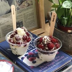 two ice cream sundaes with raspberries and whipped cream in them on a table