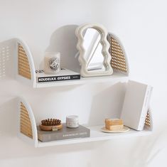 two white shelves with books, candles and other items on top of each shelf in the corner