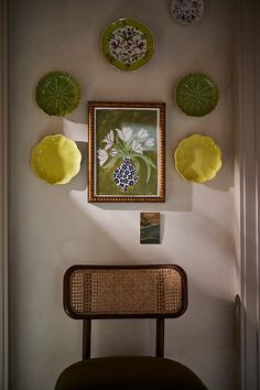 a chair in front of a wall with plates hanging on it's side and a painting above it