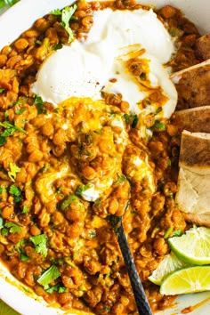 a white bowl filled with beans, rice and sour cream next to sliced limes