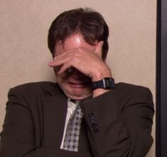 a man wearing a suit and tie with his hands on his face while sitting down