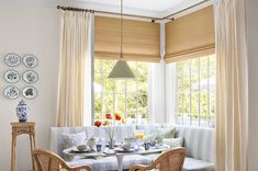 a dining room table and chairs in front of a window with white drapes on the windowsill