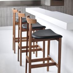 three wooden stools sitting next to a white counter with black leather seats on it