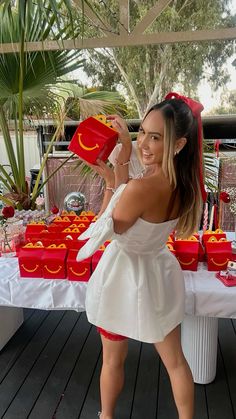 a woman in a white dress is holding a red object and posing for the camera