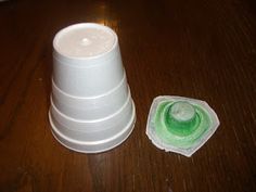 a white plastic cup sitting on top of a wooden table next to a green sponge