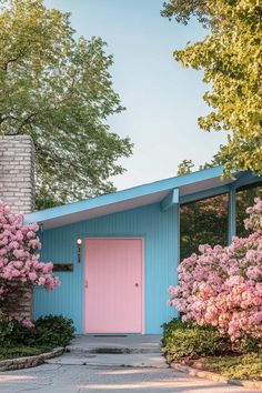 a blue house with pink door surrounded by blooming trees and bushes in front of it