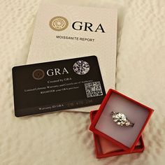 a diamond ring sitting in a red box on top of a bed next to a credit card