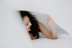 a woman laying in bed with white sheets