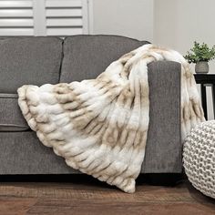 a gray couch with a white blanket on top of it next to a potted plant