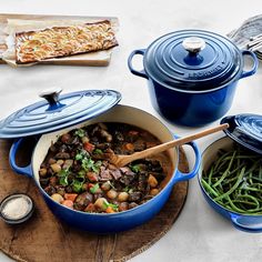 a table topped with blue pots and pans filled with food next to green beans