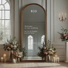 a large mirror sitting in the middle of a room filled with flowers and candles next to tall windows