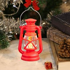 a red lantern with a lit candle in it sitting on a table next to a christmas tree