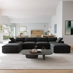 a modern living room with black couches and white carpeted flooring in front of large windows