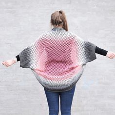 a woman with her arms spread out in front of a concrete wall wearing a knitted sweater