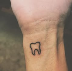 a small tooth tattoo on the wrist is shown in black ink, with an outline of a tooth