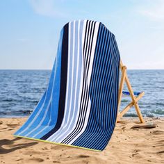 a blue and white striped beach towel sitting on top of a chair next to the ocean