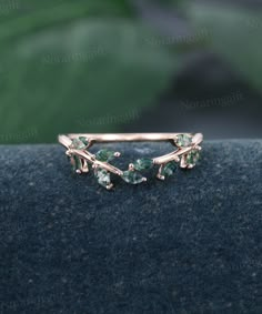 a gold ring with green stones and leaves on the front, sitting on top of a blue cloth