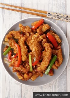 fried chicken with peppers and onions on a white plate next to chopsticks in the background