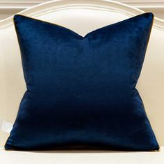 a blue velvet pillow sitting on top of a white chair with gold piping around the edges